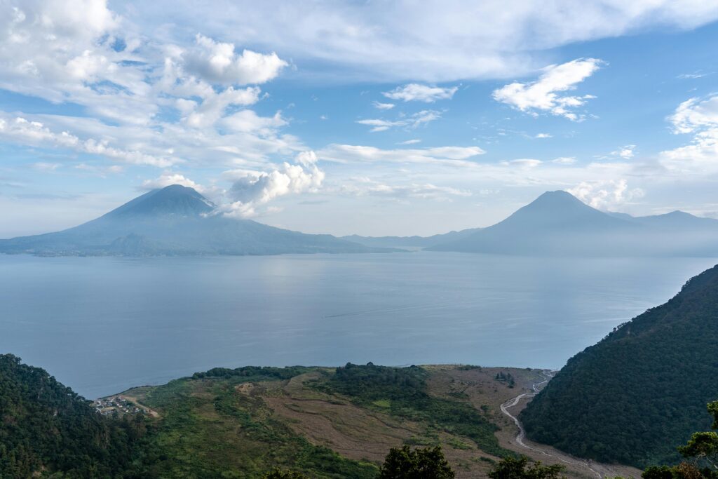 A stunning landscape of Lake Atitlán with surrounding volcanoes under a cloudy sky.