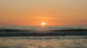 Capture the beauty of a tranquil ocean sunset with soft waves and a glowing horizon.
